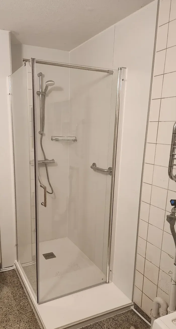 Zelfde badkamer na verbouwing: ligbad vervangen door douchecabine met glazen deuren, steunbeugel en douchebak