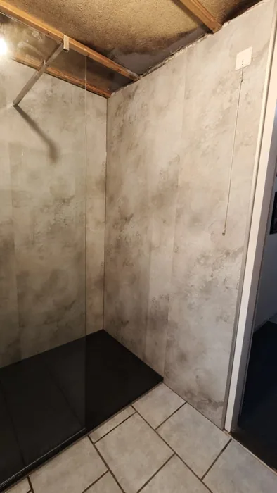 Douchehoek met gevlekte steenlook wandpanelen, glazen wand en zwarte douchebak