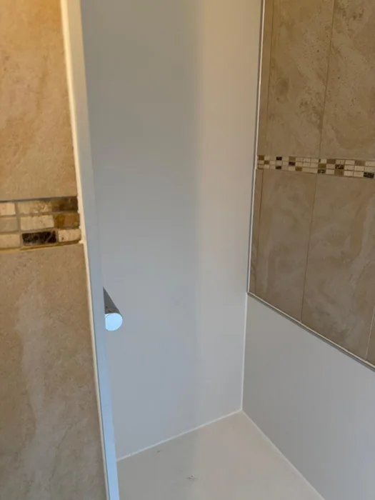 Nieuwe witte wandpanelen en douchevloer in douchenis naast bestaande beige tegels met mozaïekrand