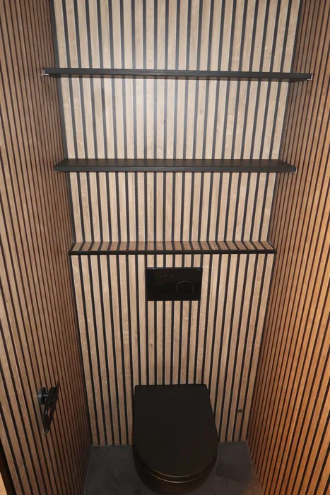 Toilet met houten lamellenwanden, zwart hangtoilet, zwarte bedieningsplaat en zwarte wandplanken